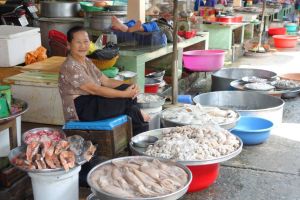 smiling Vietnamese lady selling fresh seafood including squid on the market in Vietnam