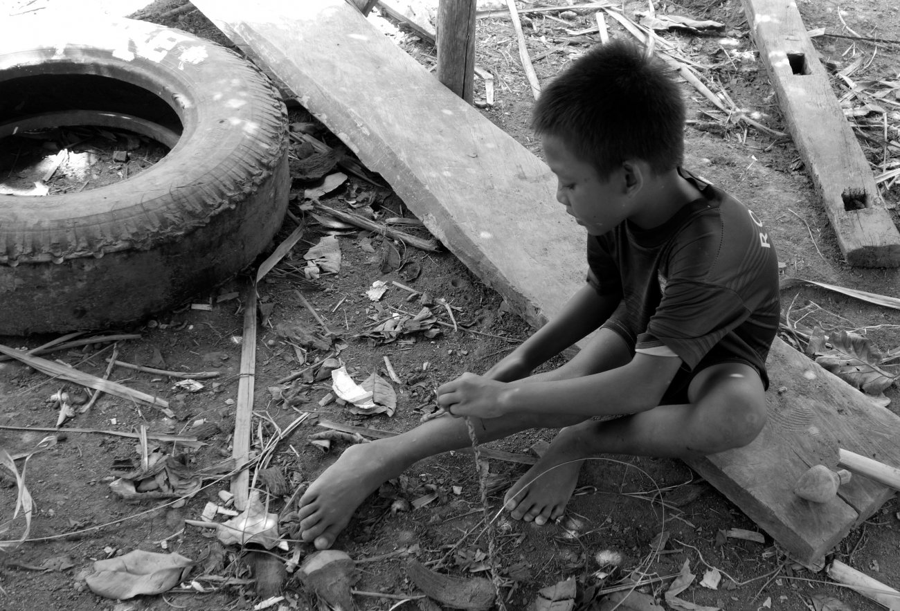 Indonesian boy makes a string for a wooden toy, Lombok, Indonesia